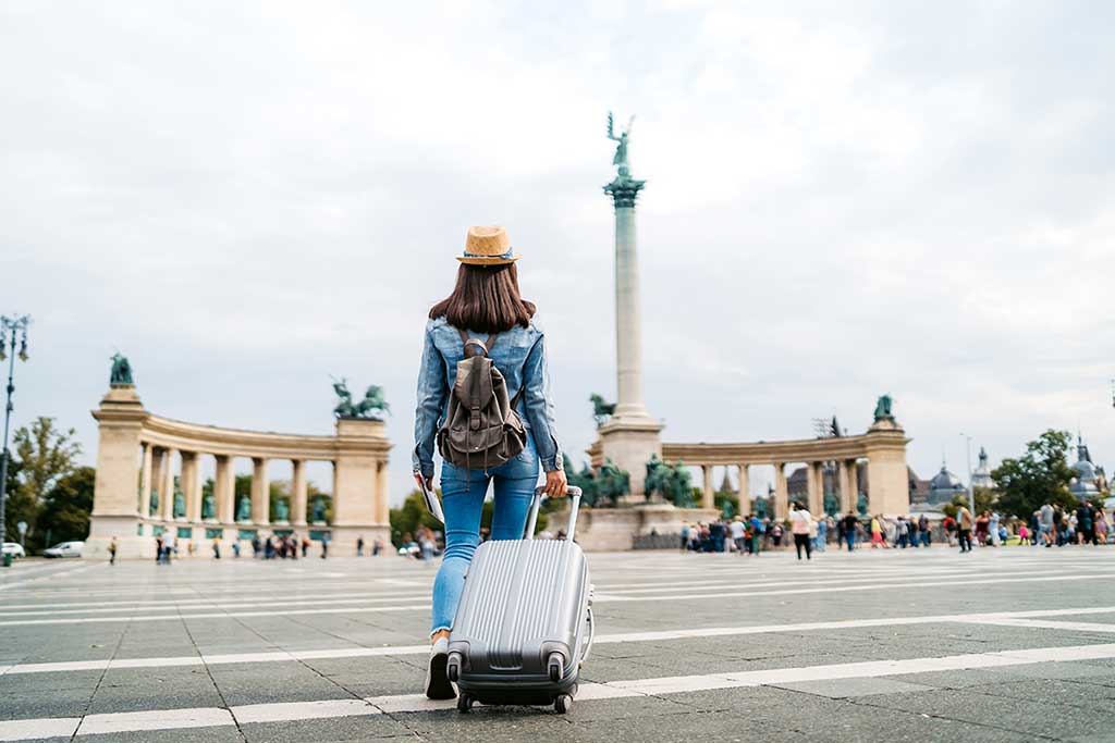 Person på reise med koffert med feriestedet i bakgrunnen.