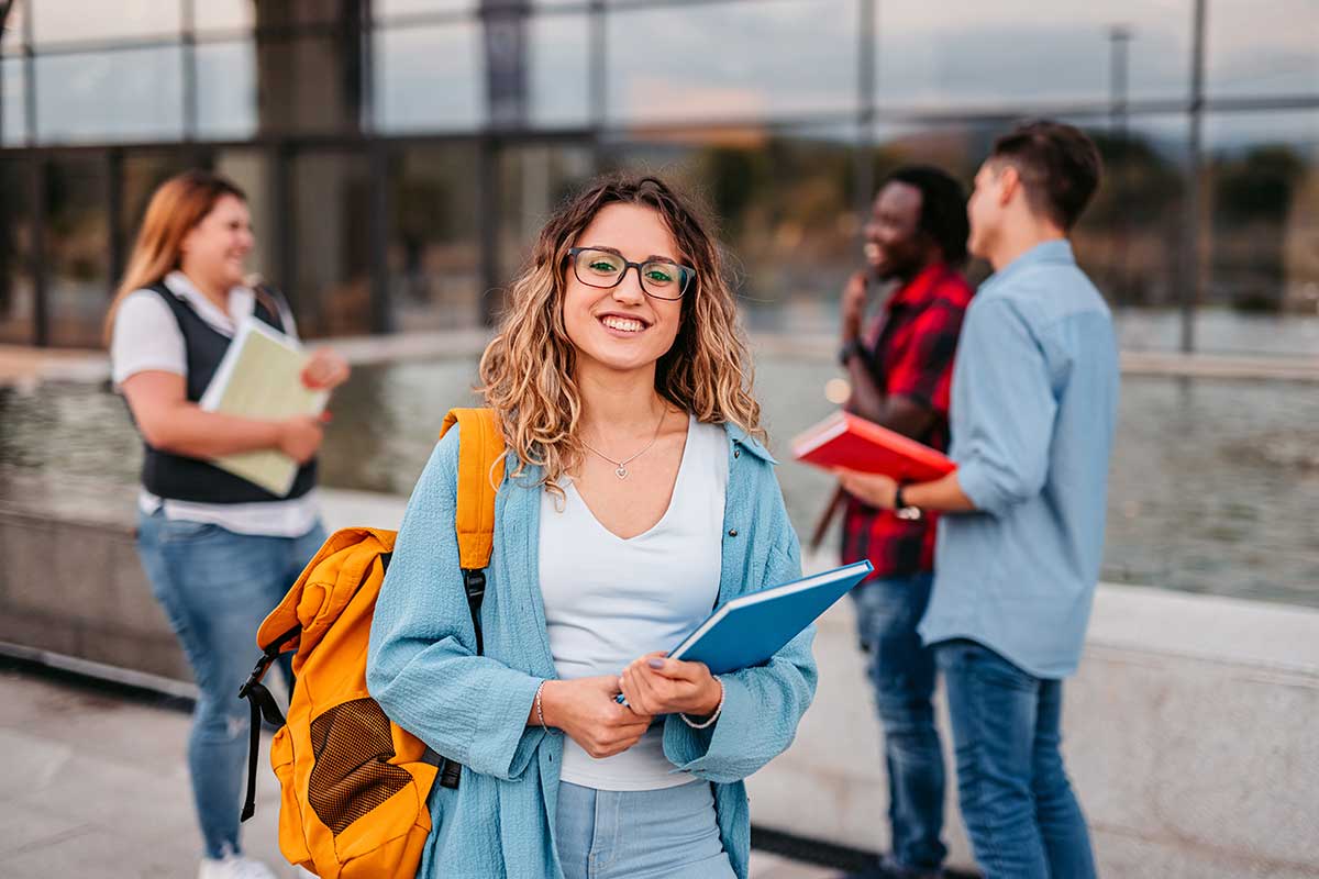 Student smilende med skolesekk, med tre andre studenter i bakgrunnen.