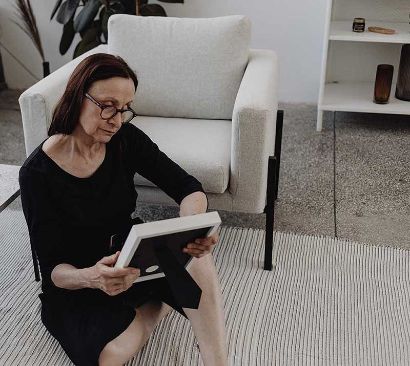 Dame sitter på gulvteppet med en bilderamme og ser på et bilde