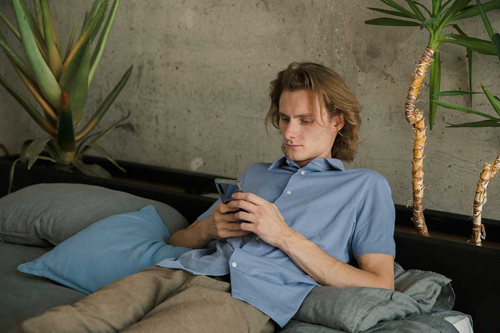 Ung mann sitter i sofaen og ser på mobilen