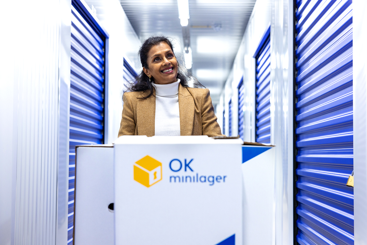 En dame har valgt OK Minilager som en smart løsning, og går med noen bokser i ett av våre lagerbygg