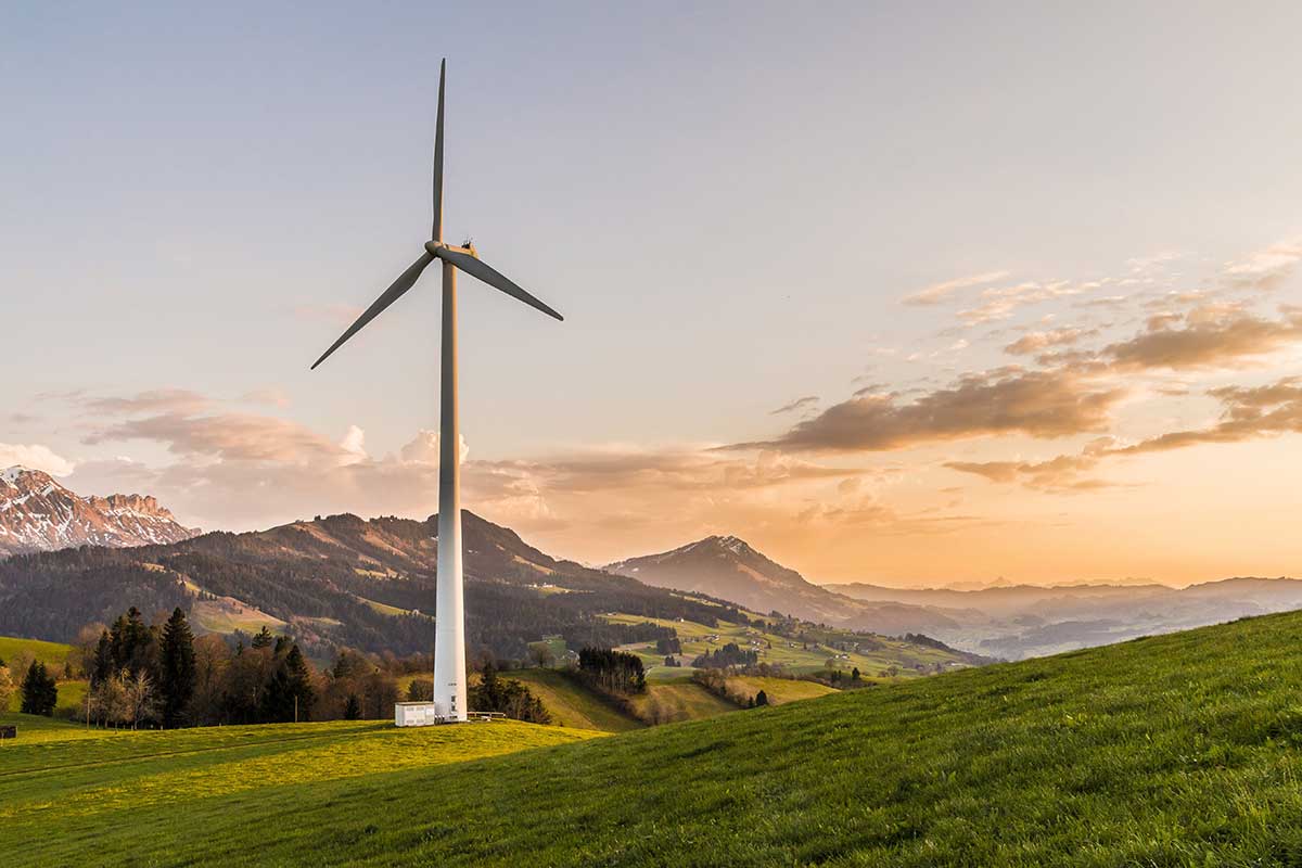 En vindmølle som gir bærekraftig energi, som står ute blant fjell og en oransje himmel