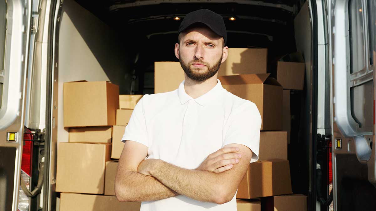 En mann fra en bedrift som står foran en lastebil med flere pakker og esker som skal på lagring