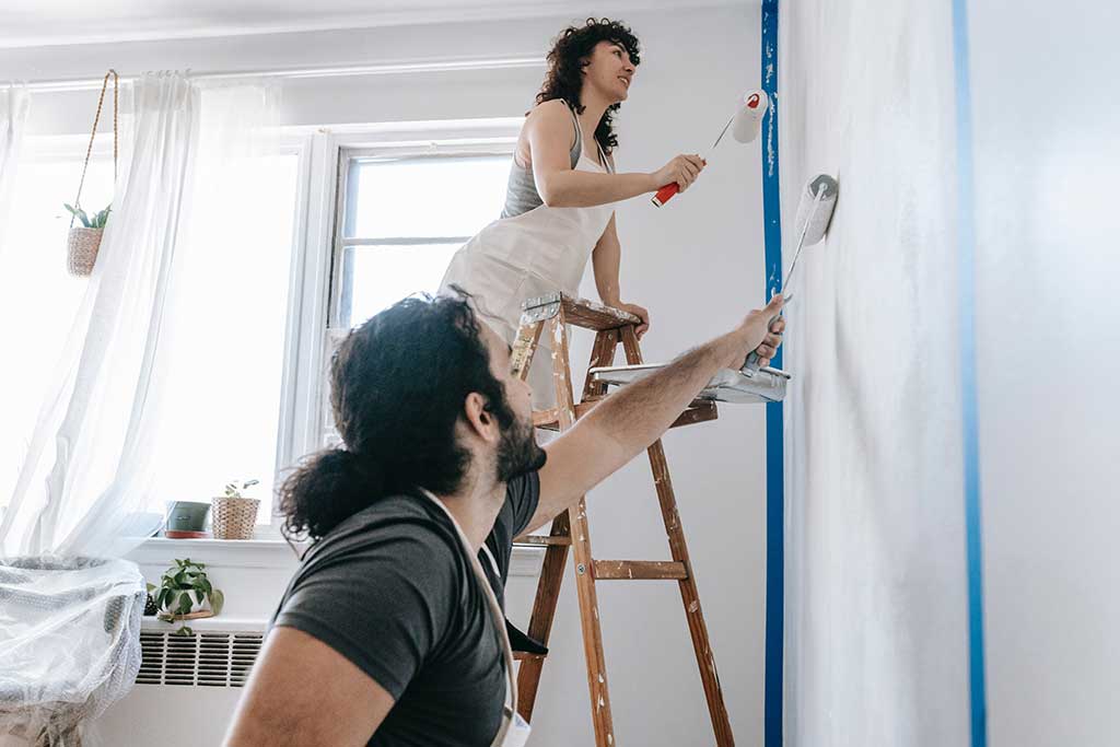 To mennesker som maler en vegg hvit, som er et riktig fargevalg basert på innredningstips for små boliger.