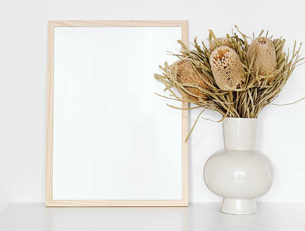 En overflate som pynter med en vase med lyse og tørket blomster, ved siden av står et speil, hvilket er gode innredningstips for en liten bolig.
