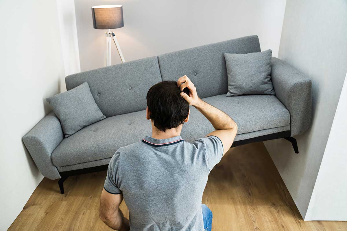 En mann som klør seg i hodet fordi han ikke har valgt riktig innredning med smarte møbler, da sofaen hans ikke får plass i en liten gang.
